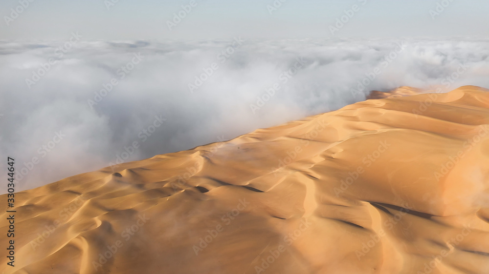 Aerial view of a massive sand dune surrounded by winter morning fog cloud in Empty Quarter. Liwa des