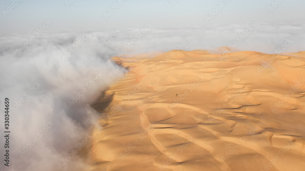 Aerial view of a massive sand dune surrounded by winter morning fog cloud in Empty Quarter. Liwa des