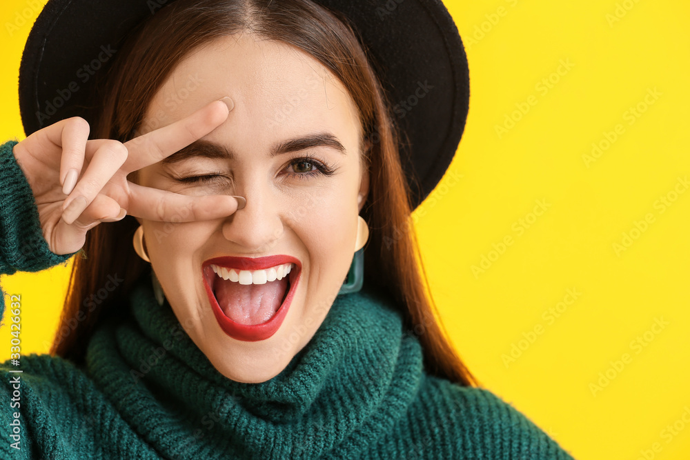 Happy young woman showing victory gesture on color background