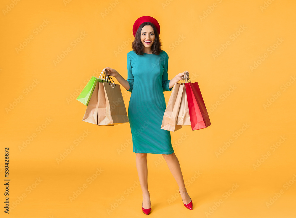 Beautiful young woman with shopping bags on color background