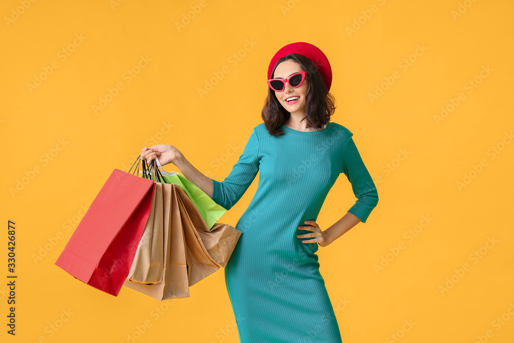 Beautiful young woman with shopping bags on color background