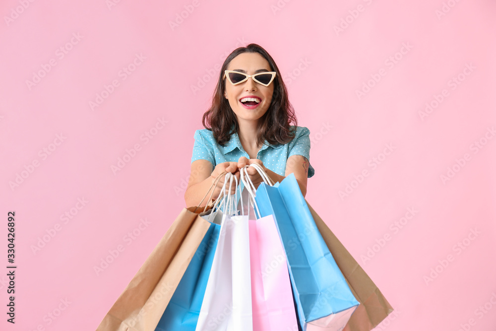 Beautiful young woman with shopping bags on color background