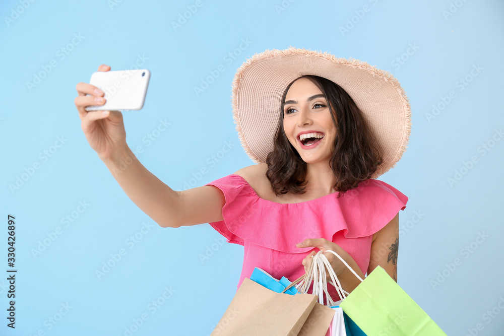 Beautiful young woman with shopping bags taking selfie on color background