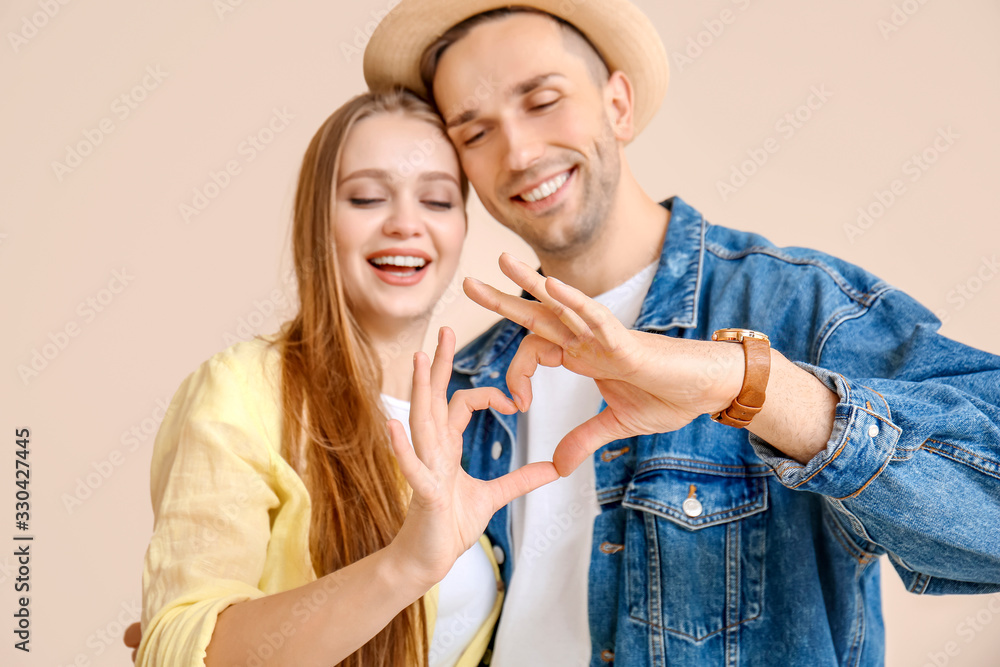 Happy young couple making heart with their hands on color background