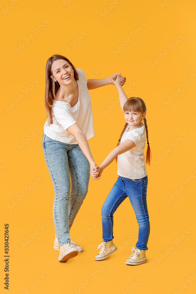 Happy mother and her little daughter dancing against color background