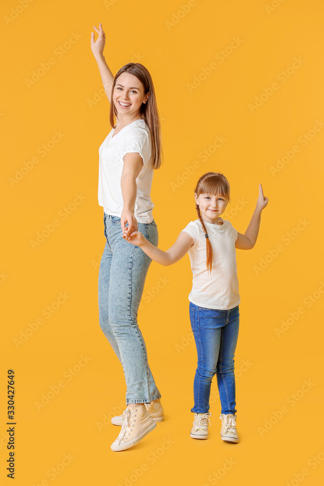 Happy mother and her little daughter dancing against color background