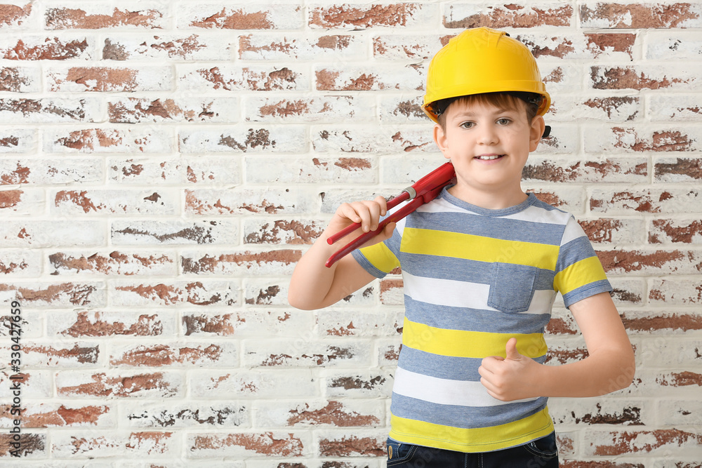 Cute little builder showing thumb-up on brick background