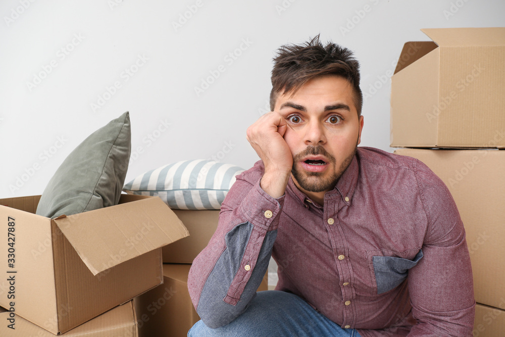 Troubled man with moving boxes on light background