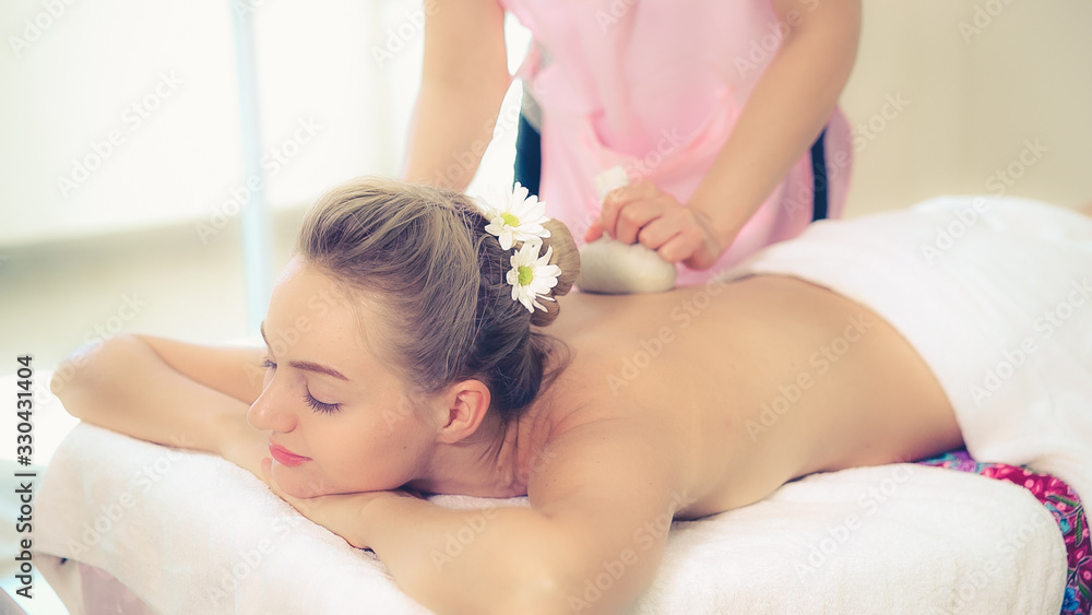 Massage therapist holds a herbal compress to do treatment to woman lying on spa bed in a luxury spa 