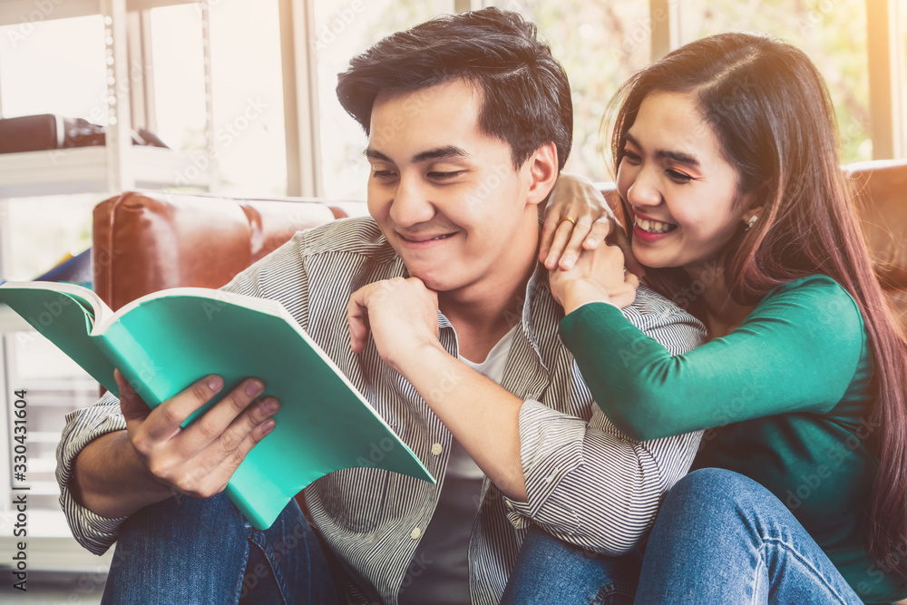 Young Asian couple reading book in living room. Love relationship and lifestyle concept.