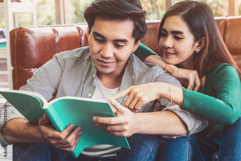 Young Asian couple reading book in living room. Love relationship and lifestyle concept.