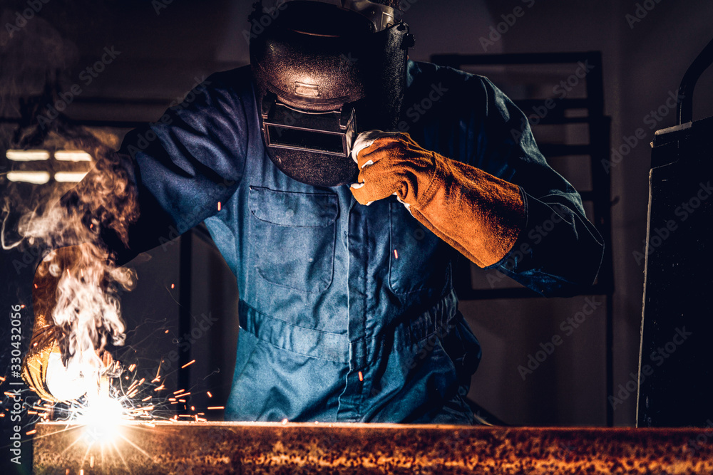 Metal welder working with arc welding machine to weld steel at factory while wearing safety equipmen