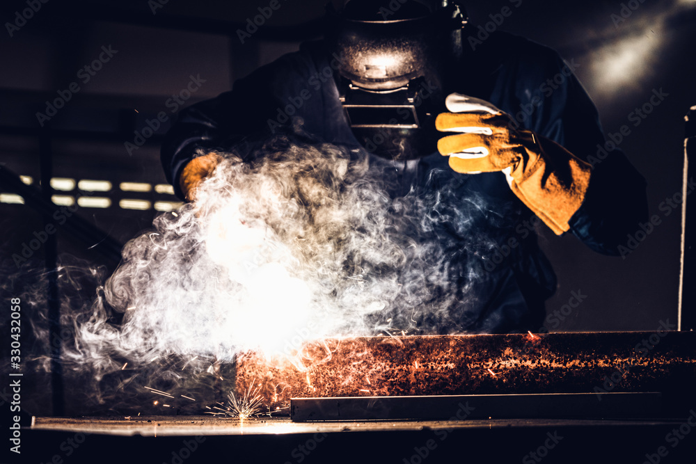 Metal welder working with arc welding machine to weld steel at factory while wearing safety equipmen