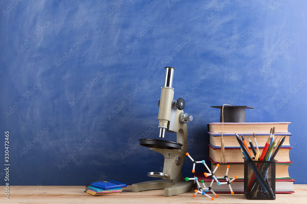 Education and sciences concept - books on the teacher desk in the auditorium, chalkboard on the back