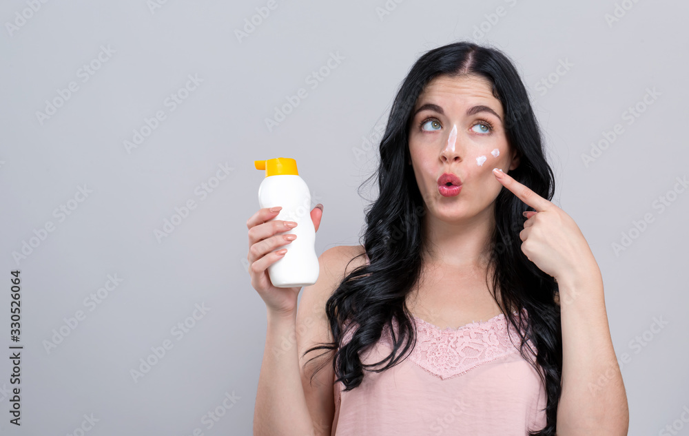 Young woman with sunscreen on a gray background