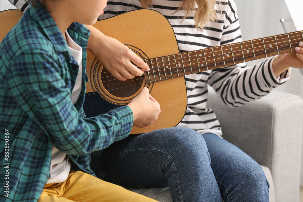 Private music teacher giving guitar lessons to little boy at home