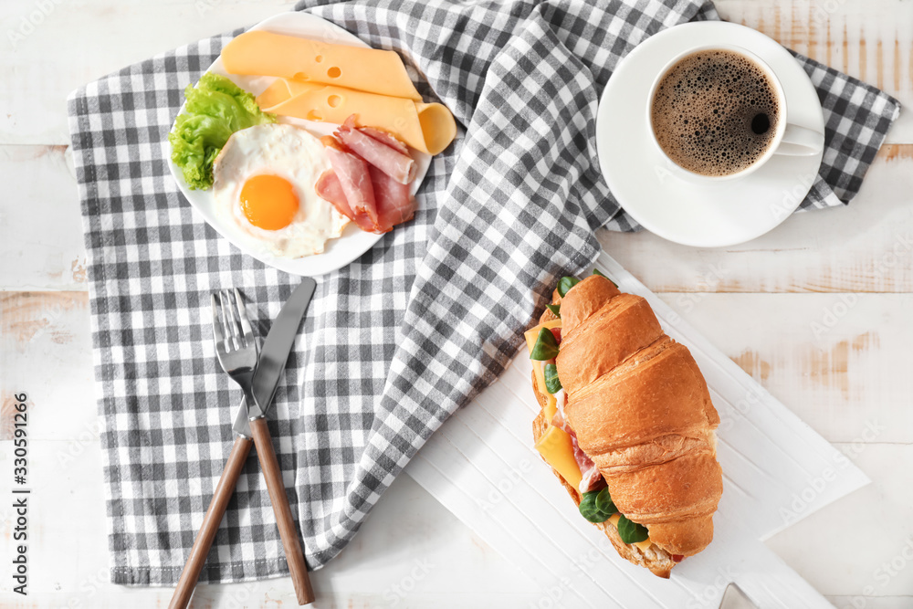 Tasty croissant sandwich with coffee and fried egg on table