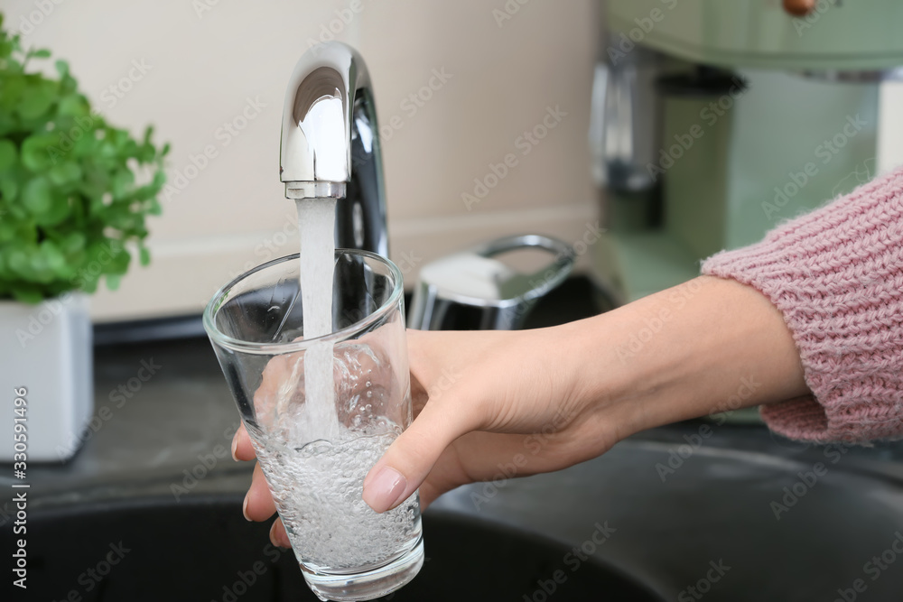 Woman filling glass with fresh water from kitchen faucet