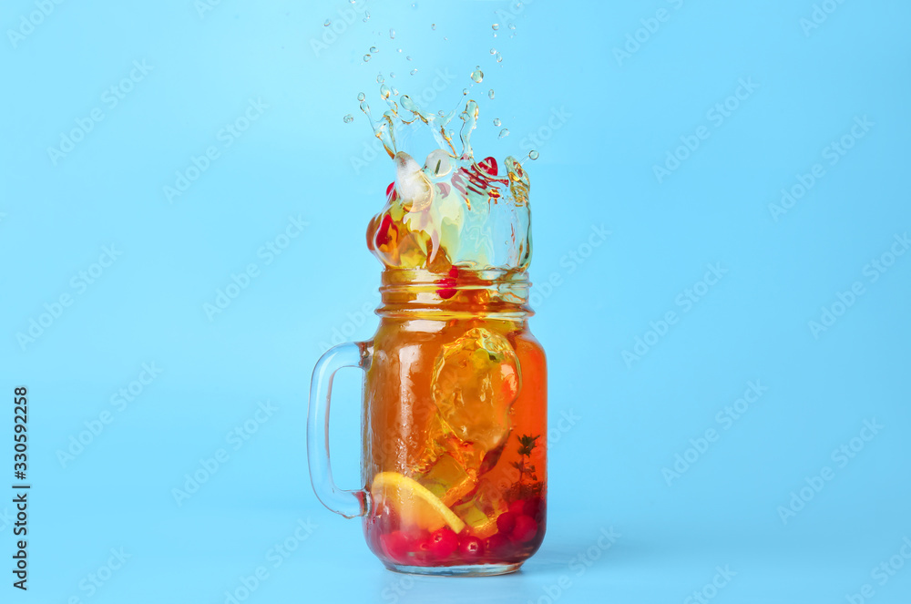 Mason jar of cold tea with splashes on color background