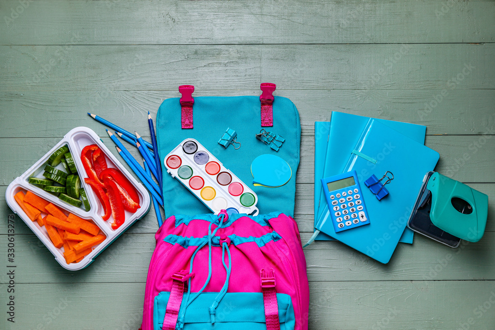 School backpack with lunch box and stationery on wooden background