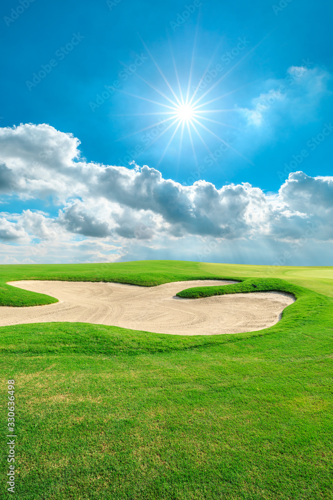 Green golf course and blue sky with white clouds.