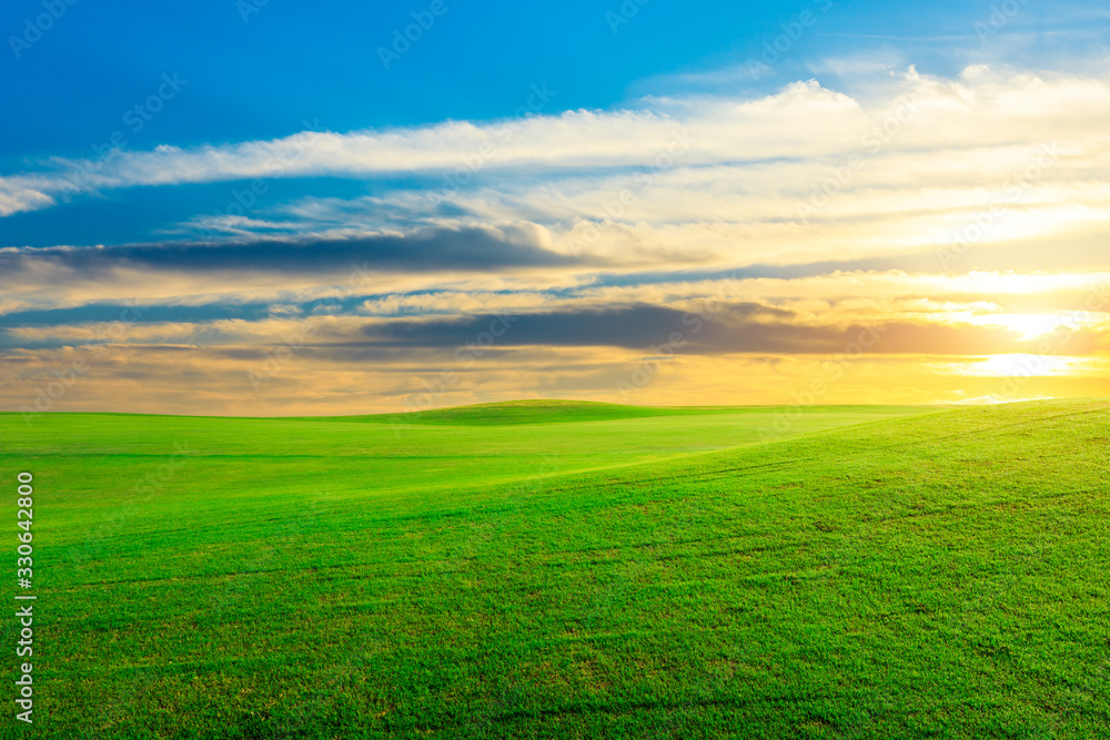 Green grass field and colorful sky clouds at sunset.