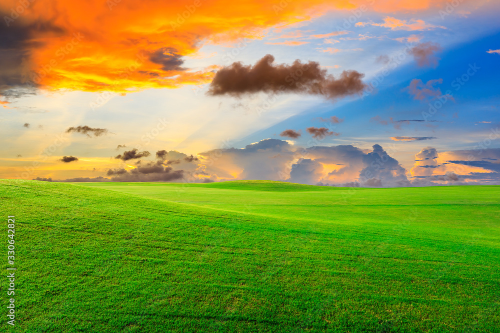 Green grass field and colorful sky clouds at sunset.