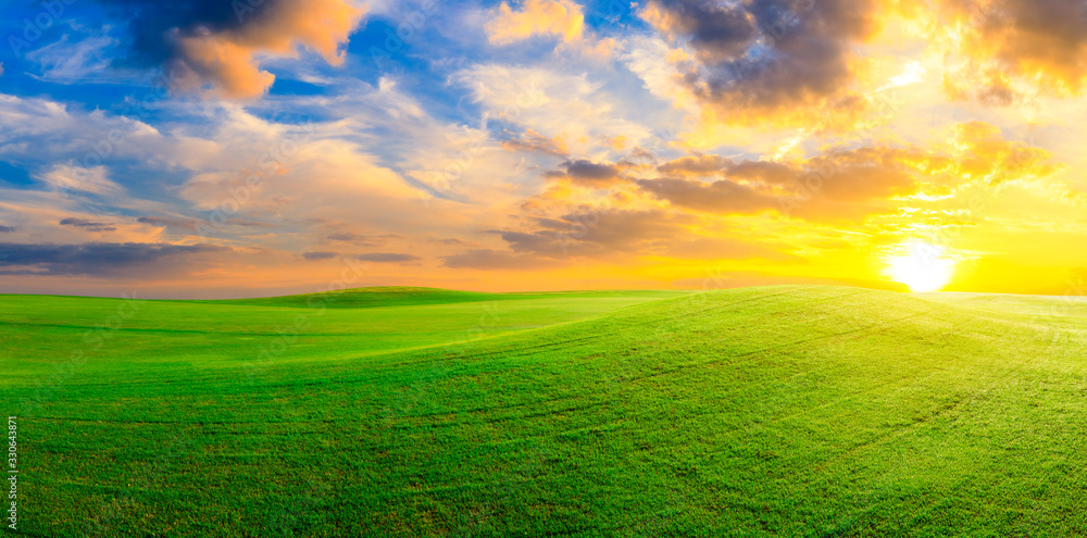 Green grass field and colorful sky clouds at sunset,panoramic view.