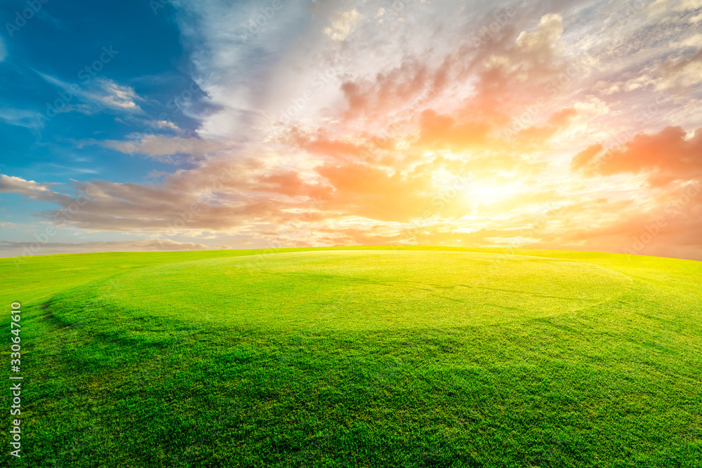 Green grass field and colorful sky clouds at sunset.