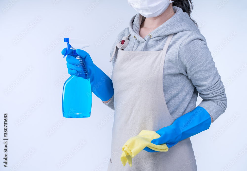 Young woman housekeeper in apron is doing cleaning with blue gloves, wet yellow rag, spraying bottle