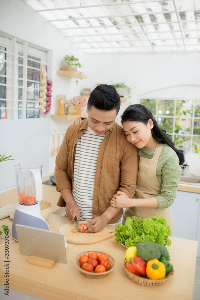 一对漂亮的年轻夫妇在平板电脑上按照食谱一起烹饪的肖像