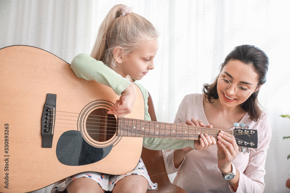 Private music teacher giving guitar lessons to little girl at home