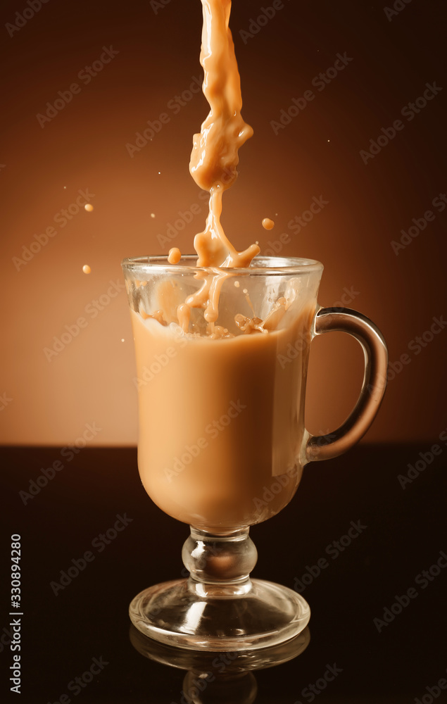 Pouring of coffee with milk into glass cup on dark background