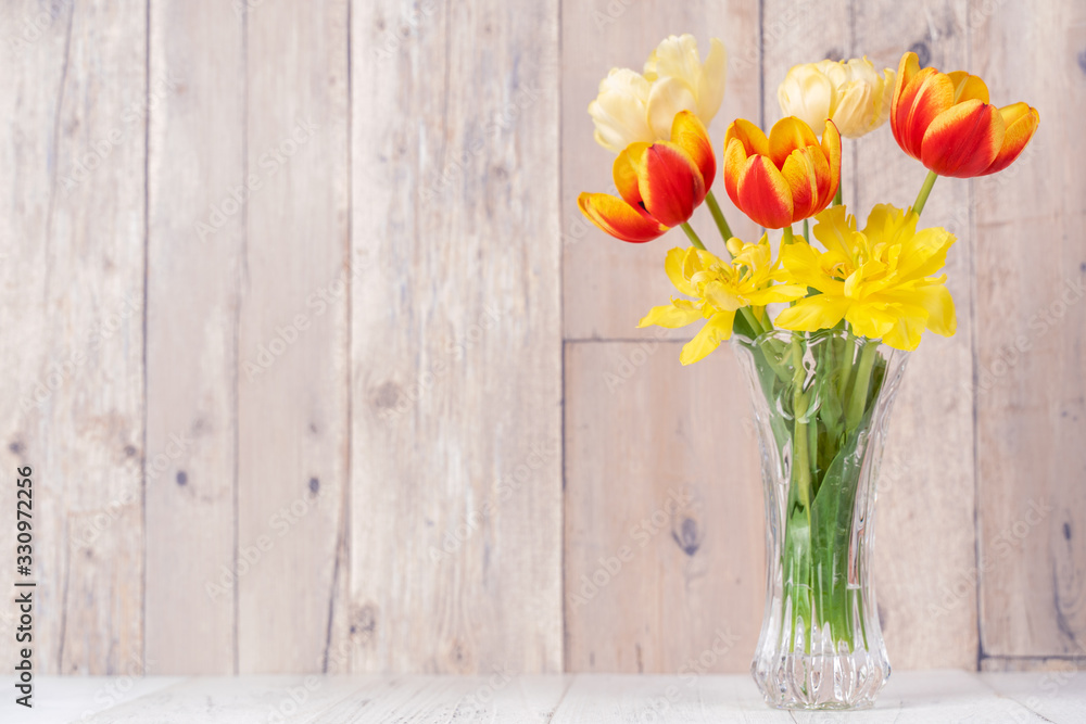 Tulip flower arrangement in glass vase with heart greeting, watering can decor on wooden table backg