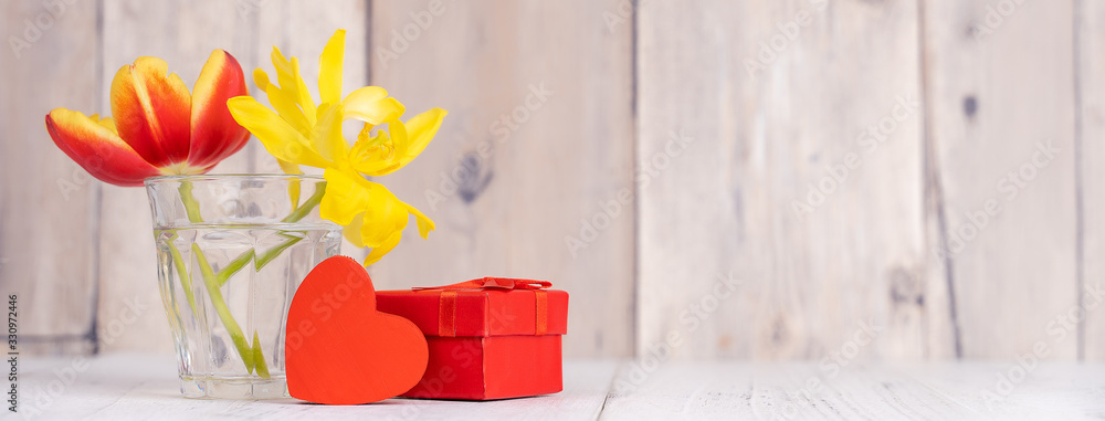 Tulip flower arrangement in glass vase with heart greeting, watering can decor on wooden table backg