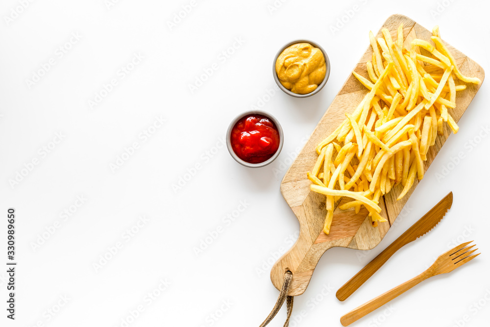 Fast food restaurant concept. French fries on cutting board near sauces on white table top-down copy