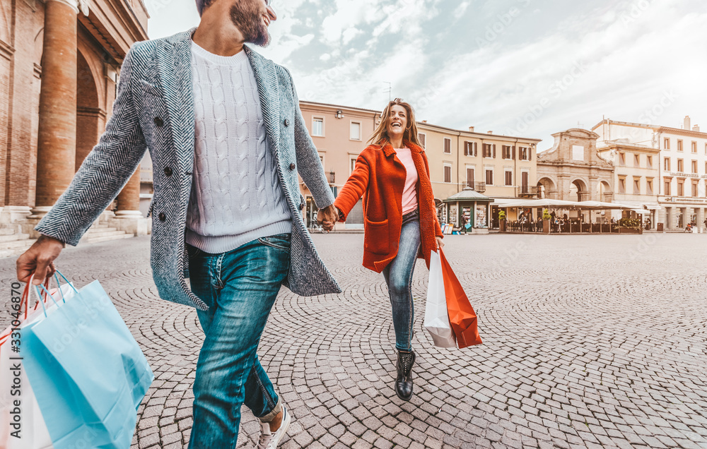 Beautiful loving couple carrying shopping bags running in the city street and enjoying together vaca