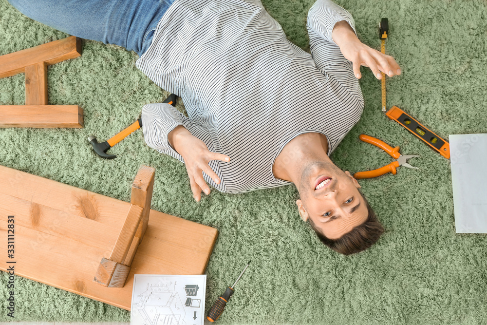 Stressed man assembling furniture at home, top view