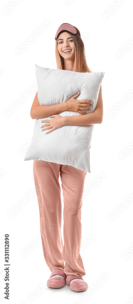 Portrait of young woman in pajamas, with sleep mask and pillow on white background