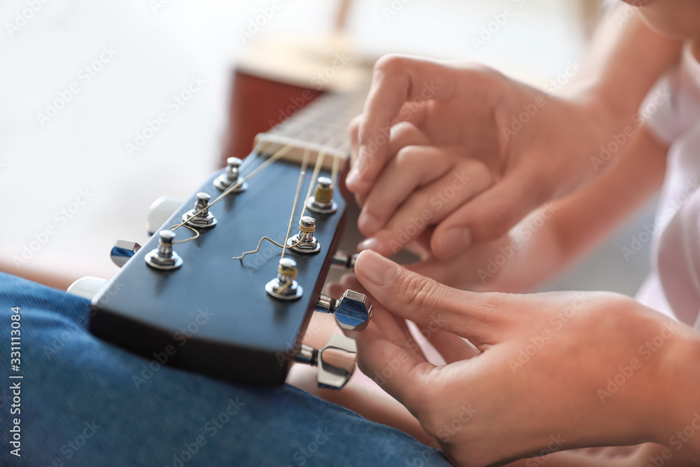 Private music teacher giving guitar lessons to little girl at home, closeup