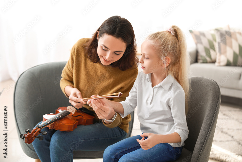 Private music teacher giving violin lessons to little girl at home