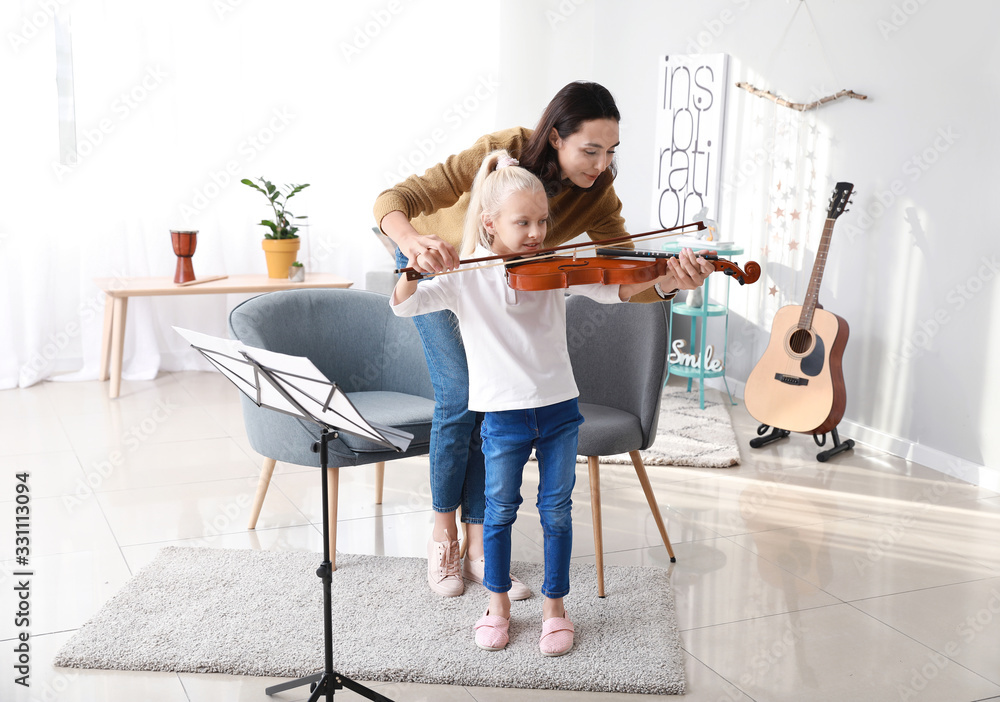 Private music teacher giving violin lessons to little girl at home