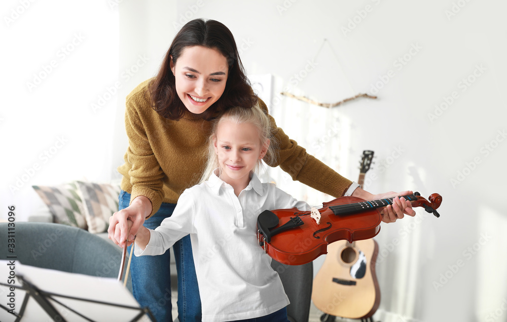 Private music teacher giving violin lessons to little girl at home