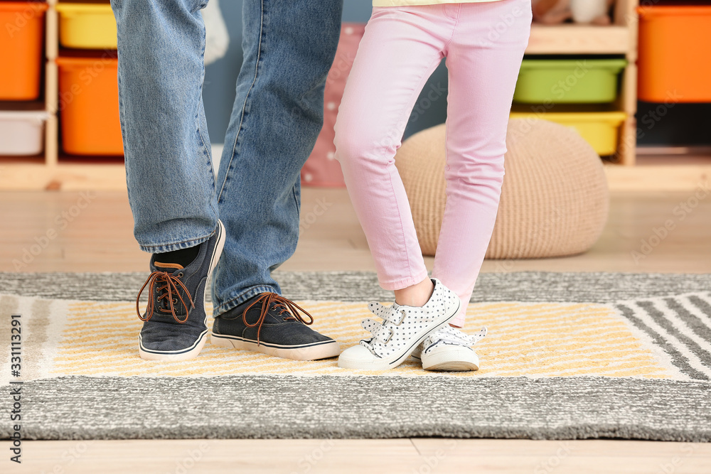 Legs of father and his little daughter dancing at home