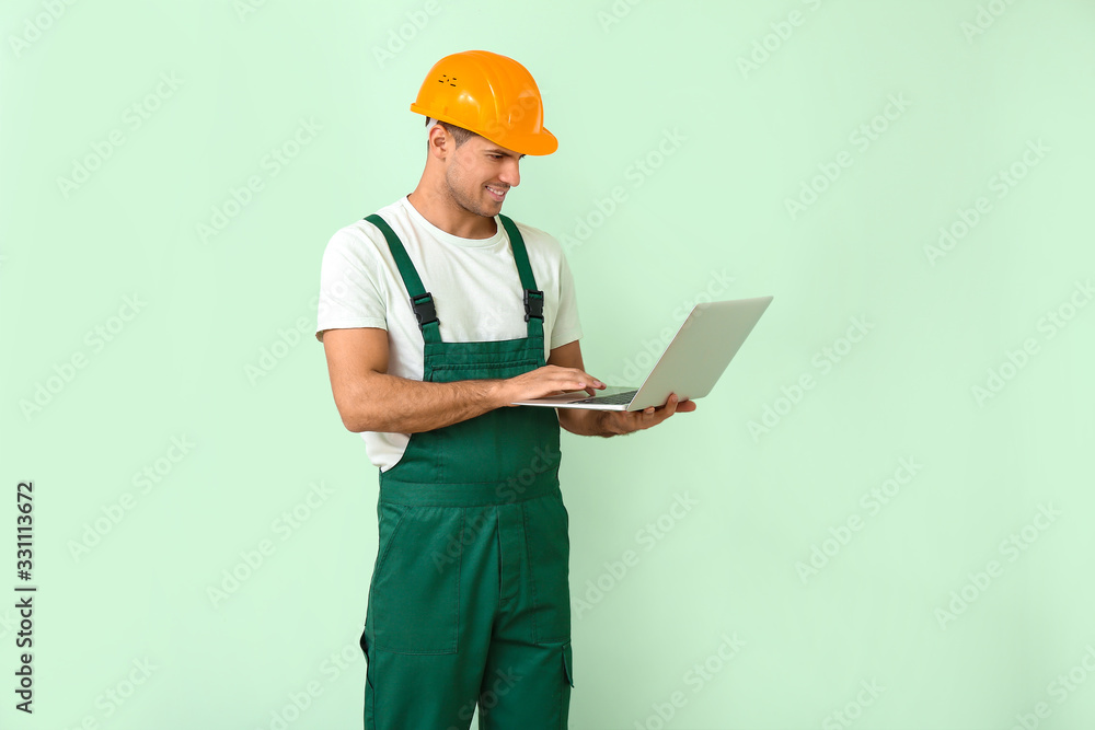 Handsome male worker with laptop on color background