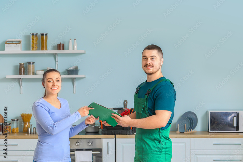 Handsome plumber giving documents to young woman after repairing sink in kitchen