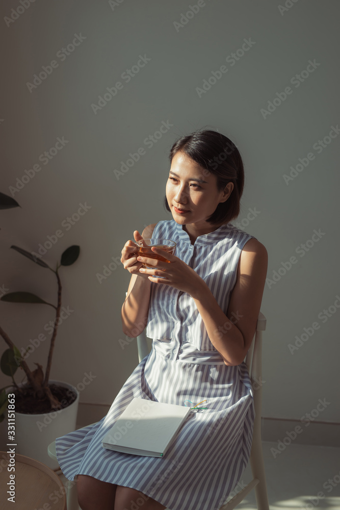 Young woman reading book near window at home