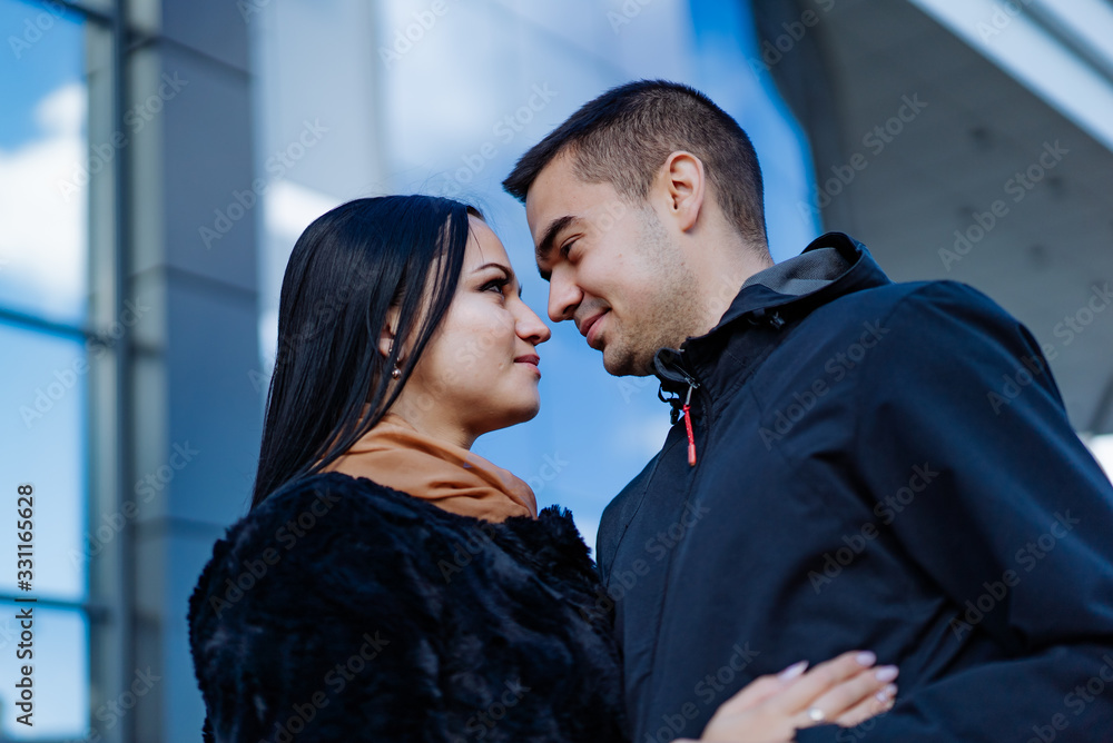 一对情侣在有镜子窗户的建筑背景上拥抱。男人和女人坠入爱河。亲密-