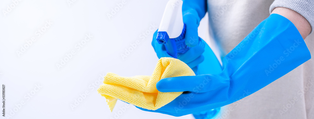 Young woman housekeeper in apron is cleaning, wiping down table surface with blue gloves, wet yellow