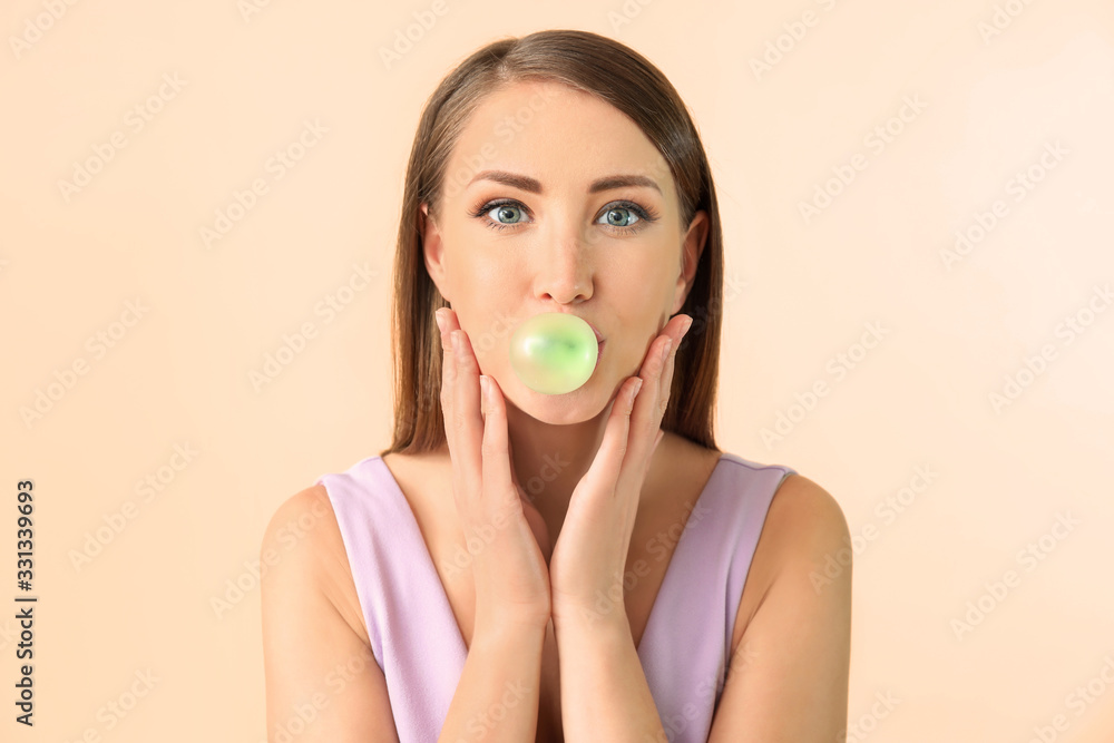 Beautiful young woman with chewing gum on color background